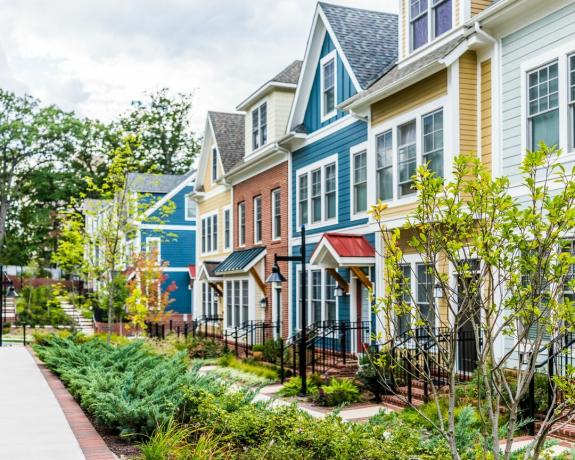 Fila de coloridas, rojas, amarillas, azules, blancas, casas residenciales pintadas de verde, casas, casas con jardines de patio de ladrillo en verano