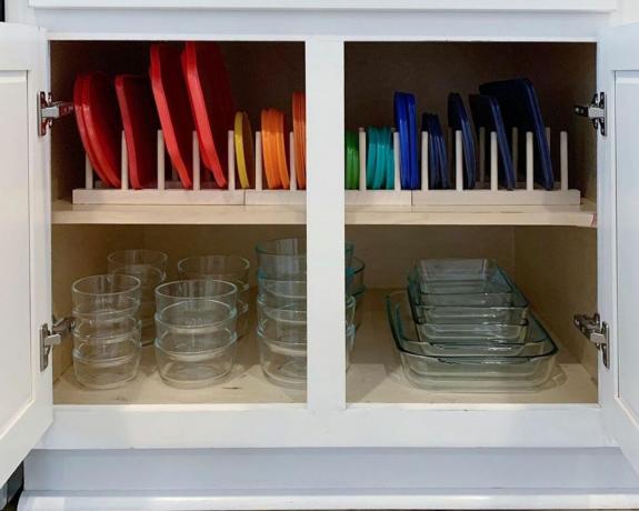 Une armoire avec des Tupperware en verre et des couvercles colorés organisés par ordre de couleur dans un support en bois