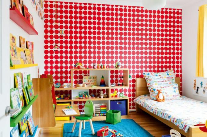Kamar anak dengan wallpaper jerawatan merah dan meja yang digantung di dinding