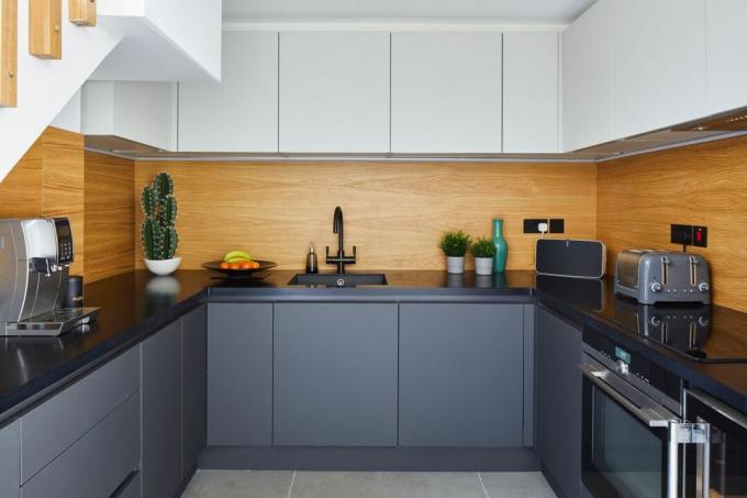 cocina en forma de U con placa para salpicaduras de madera, gabinetes de color gris carbón y gabinetes blancos en una casa moderna
