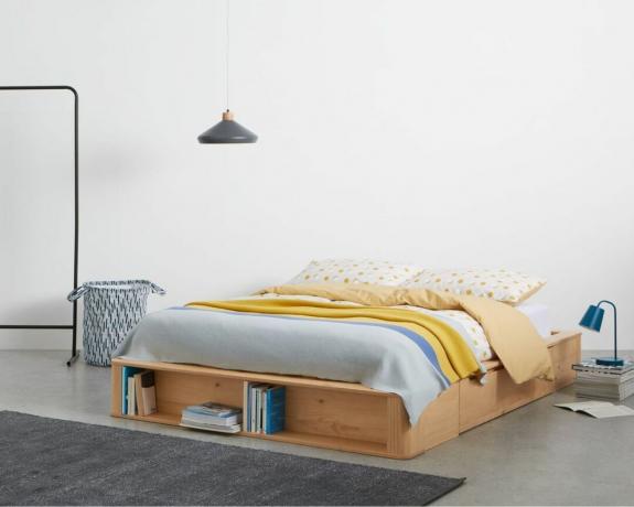 MADE.com Kano kaheinimeseplatvormiga voodi koos hoiulinkidega põrandal magamistoas, kus on sinine ja kollane voodipesu