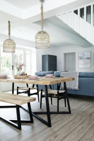 Кухня-їдальня-вітальня з чорним і дерев'яним обіднім набором в промисловому стилі, ротанговими підвісними світильниками, синім диваном і білими стінами